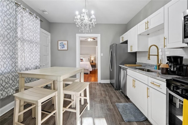 kitchen featuring sink, appliances with stainless steel finishes, white cabinets, ceiling fan with notable chandelier, and backsplash