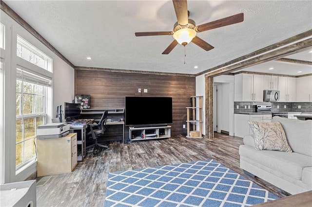 living room with ceiling fan, hardwood / wood-style floors, beam ceiling, a textured ceiling, and wood walls