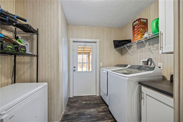 clothes washing area featuring washing machine and dryer, cabinets, a textured ceiling, dark hardwood / wood-style flooring, and wood walls