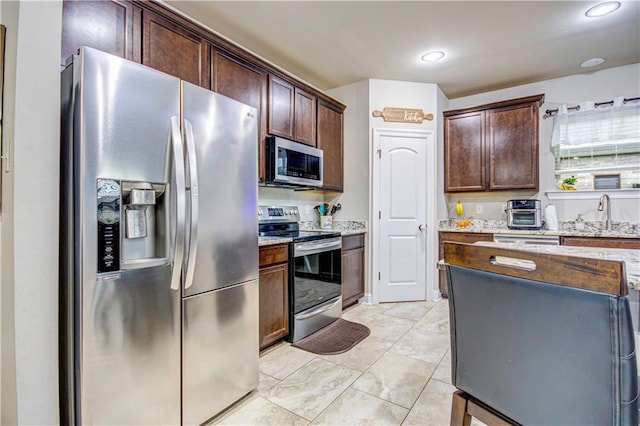 kitchen with sink, dark brown cabinets, stainless steel appliances, and light stone countertops