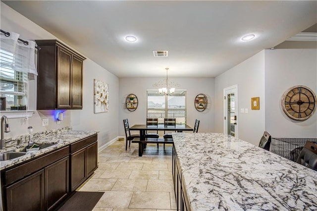 kitchen featuring decorative light fixtures, sink, dark brown cabinetry, light stone counters, and an inviting chandelier