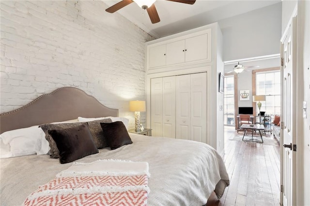 bedroom featuring a closet, a towering ceiling, ceiling fan, brick wall, and hardwood / wood-style floors