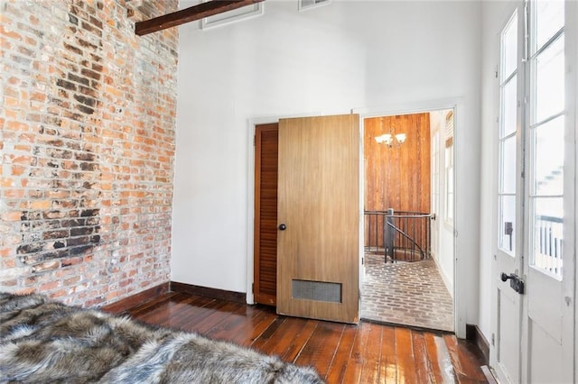 interior space with an inviting chandelier, dark wood-type flooring, brick wall, and a high ceiling