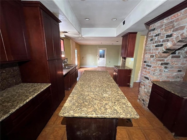 kitchen with sink, light stone counters, tasteful backsplash, a raised ceiling, and a kitchen island