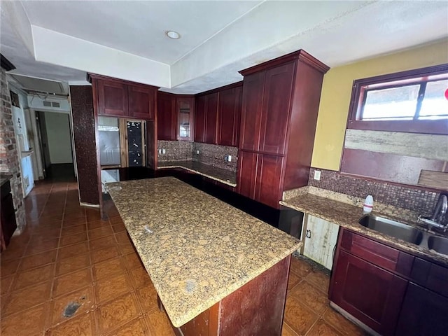 kitchen featuring sink, dark tile patterned flooring, decorative backsplash, a center island, and light stone counters