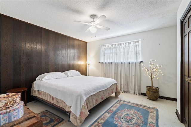 bedroom featuring ceiling fan, a textured ceiling, and wood walls