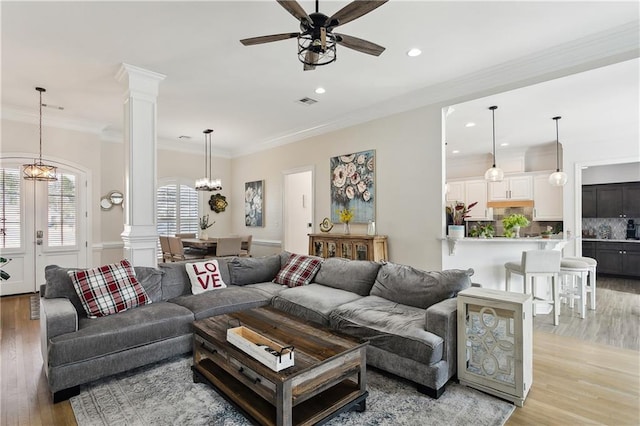 living room featuring crown molding, ceiling fan with notable chandelier, light hardwood / wood-style floors, and decorative columns