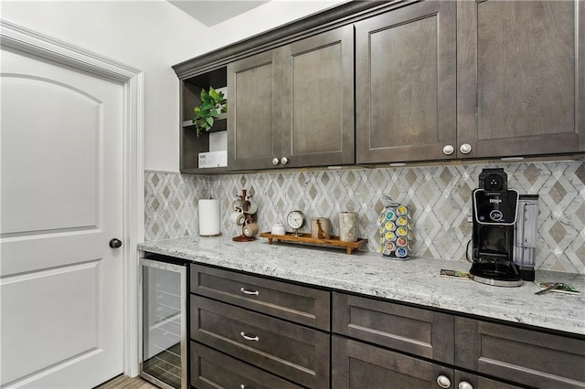 kitchen with wine cooler, dark brown cabinetry, light stone countertops, and decorative backsplash