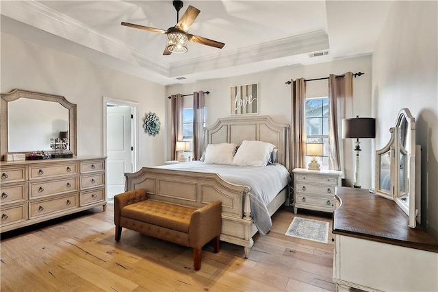 bedroom featuring multiple windows, a raised ceiling, ornamental molding, and light wood-type flooring