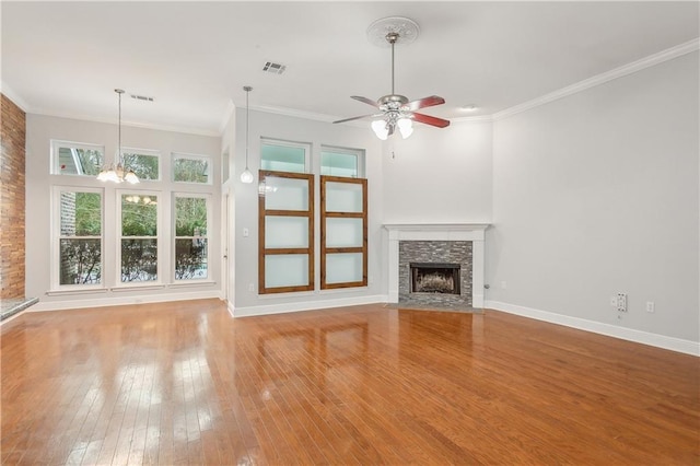 unfurnished living room with crown molding, wood-type flooring, a stone fireplace, and ceiling fan with notable chandelier