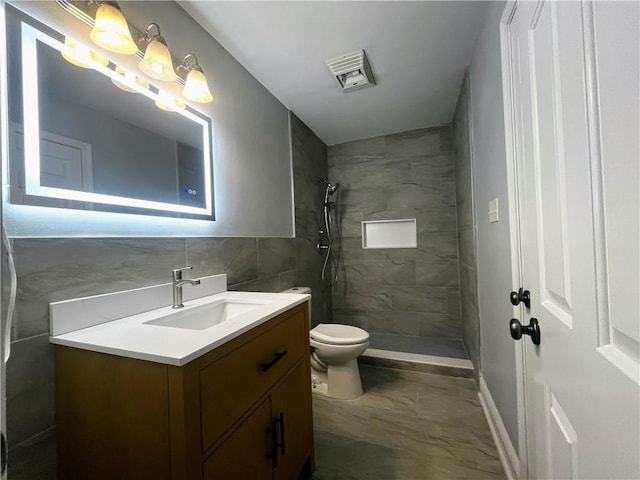 bathroom featuring vanity, tile walls, toilet, and tiled shower