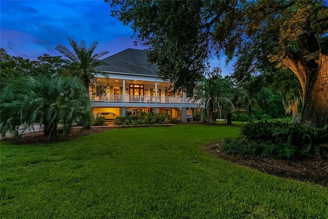 back house at dusk with a yard and a balcony