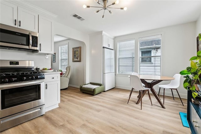 kitchen with white cabinetry, appliances with stainless steel finishes, light hardwood / wood-style flooring, and a notable chandelier