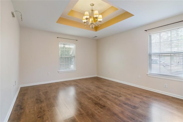 empty room with a tray ceiling, dark wood-type flooring, and a chandelier