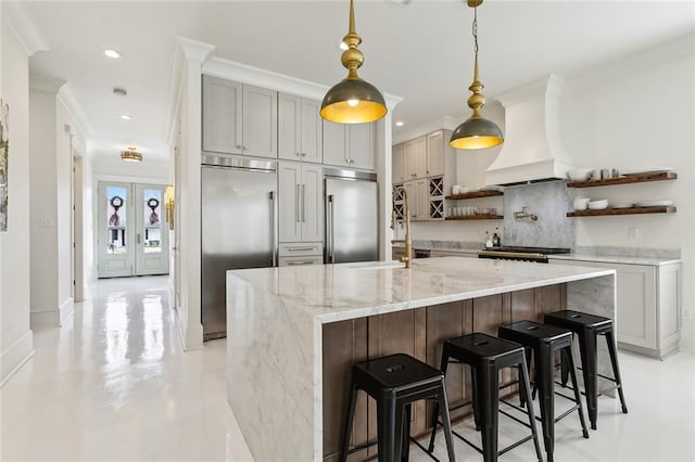 kitchen with built in refrigerator, a breakfast bar area, custom range hood, and a large island with sink