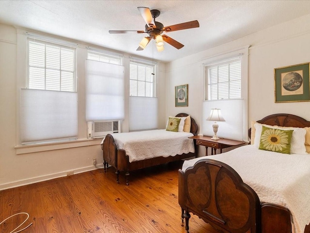 bedroom with multiple windows, cooling unit, wood finished floors, and a ceiling fan