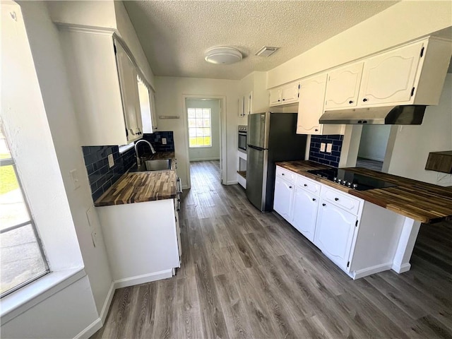1751 Holiday Dr, New Orleans, LA 70114 - kitchen with under cabinet range hood, black electric stovetop, wooden counters, visible vents, and freestanding refrigerator