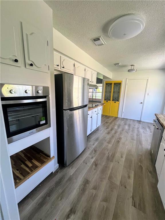 1751 Holiday Dr, New Orleans, LA 70114 - kitchen with white cabinetry, a textured ceiling, stainless steel appliances, visible vents, and light wood-style floors