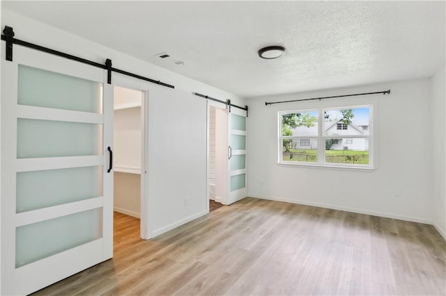 1751 Holiday Dr, New Orleans, LA 70114 - unfurnished bedroom featuring baseboards, a barn door, a textured ceiling, and wood finished floors