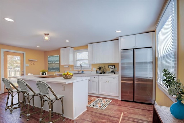 kitchen featuring a kitchen island, white cabinetry, sink, a breakfast bar area, and built in refrigerator