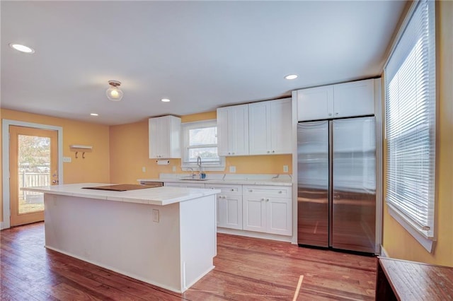 kitchen featuring sink, built in refrigerator, a kitchen island, light hardwood / wood-style floors, and white cabinets