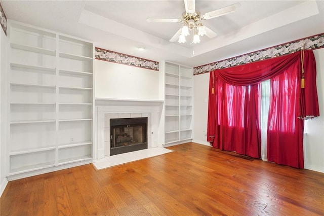 unfurnished living room with hardwood / wood-style floors, a fireplace, a raised ceiling, and ceiling fan