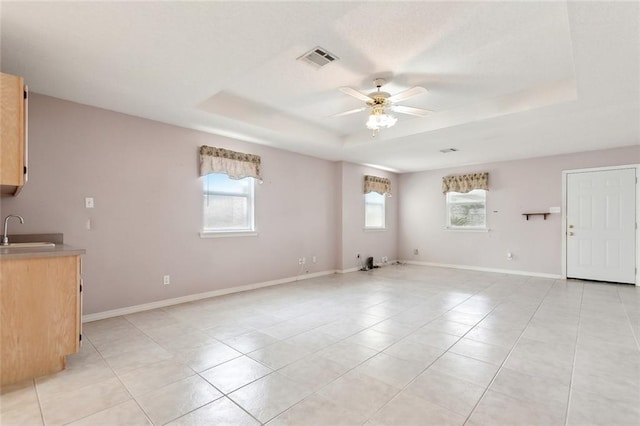 interior space with light tile patterned flooring, sink, ceiling fan, and a tray ceiling