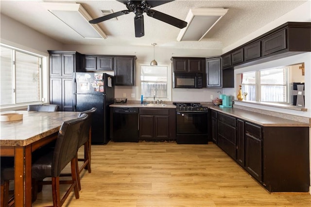 kitchen featuring sink, dark brown cabinets, light wood-type flooring, hanging light fixtures, and black appliances