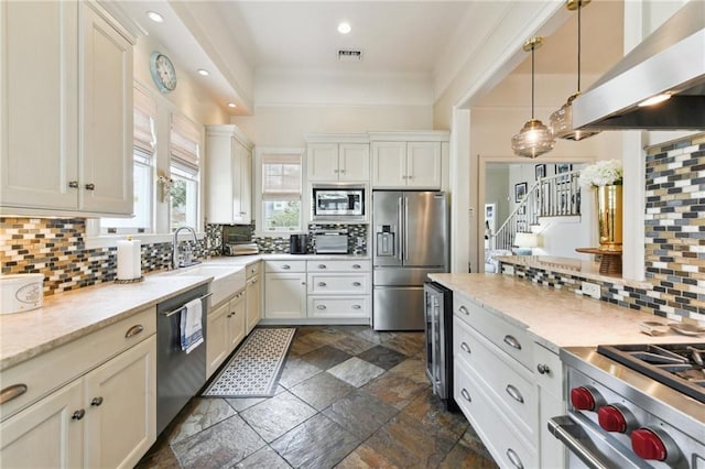 kitchen featuring sink, hanging light fixtures, premium appliances, white cabinets, and exhaust hood