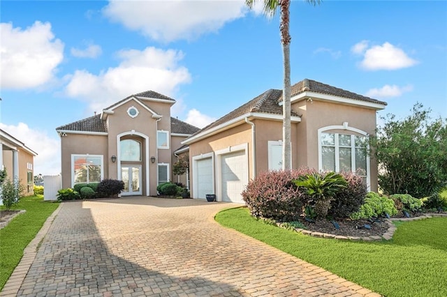 mediterranean / spanish home with stucco siding, an attached garage, decorative driveway, and french doors