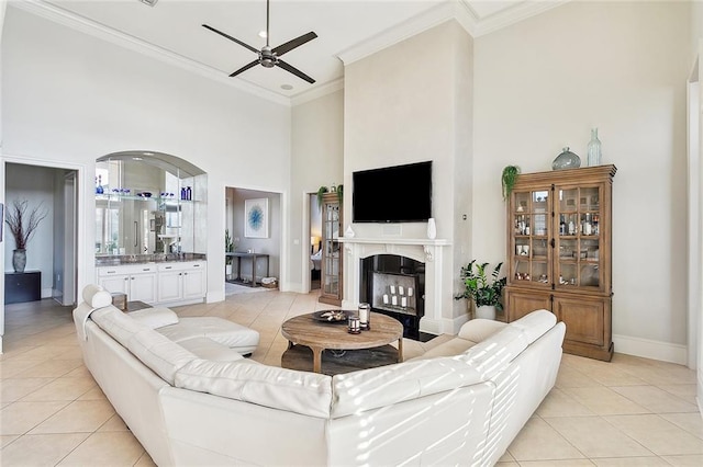 living area with crown molding, light tile patterned floors, a ceiling fan, and a towering ceiling