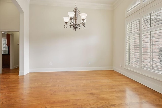 empty room with ornamental molding, a chandelier, and light hardwood / wood-style flooring