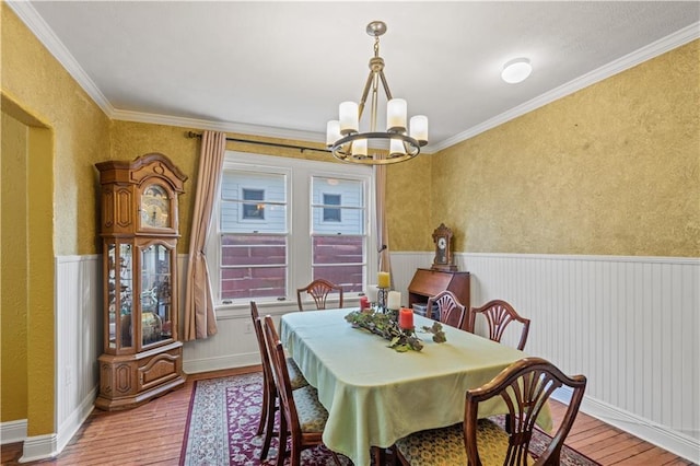 dining room featuring an inviting chandelier, ornamental molding, wainscoting, and hardwood / wood-style flooring