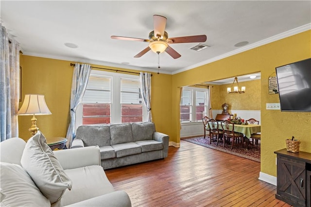 living area featuring visible vents, ornamental molding, ceiling fan with notable chandelier, wood-type flooring, and baseboards