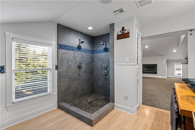 full bath with visible vents, a fireplace, tiled shower, and wood finished floors