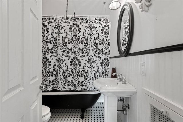 full bath featuring a shower with shower curtain, toilet, a tub, and wainscoting