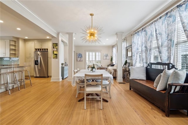 dining space featuring an inviting chandelier, crown molding, light hardwood / wood-style floors, and ornate columns