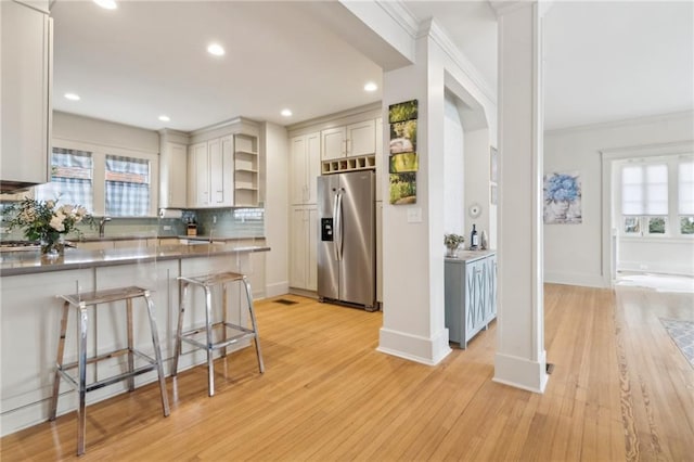 kitchen with a breakfast bar area, crown molding, tasteful backsplash, stainless steel fridge, and white cabinets