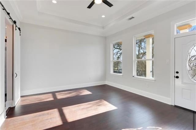 entrance foyer with dark hardwood / wood-style flooring, ceiling fan, a tray ceiling, crown molding, and a barn door