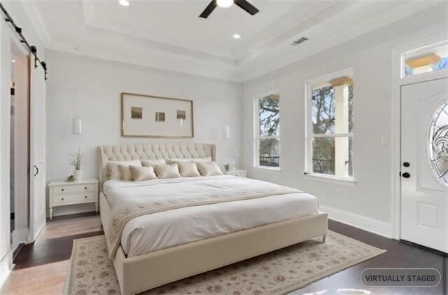 bedroom featuring dark hardwood / wood-style floors, ceiling fan, a tray ceiling, and a barn door