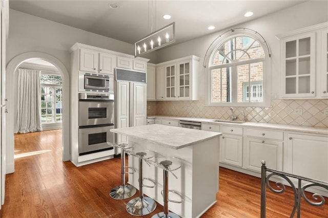 kitchen with pendant lighting, sink, white cabinetry, stainless steel appliances, and a center island