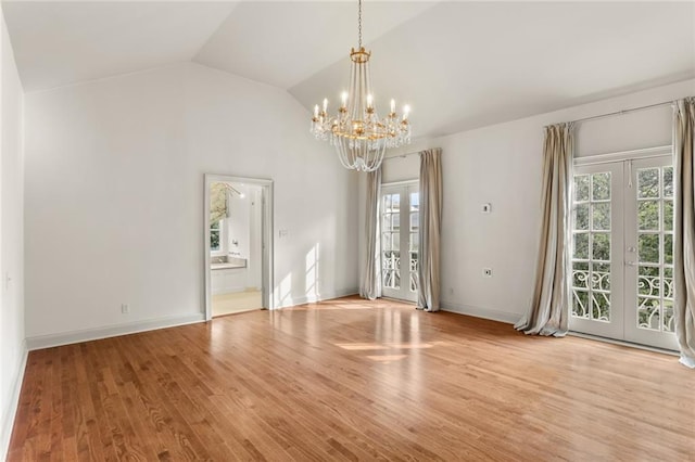 unfurnished room featuring a notable chandelier, vaulted ceiling, light hardwood / wood-style floors, and french doors