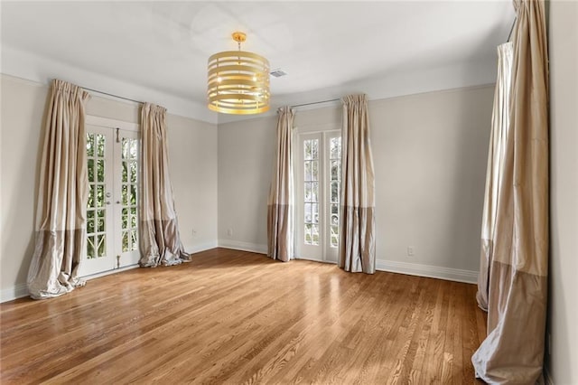 unfurnished room featuring a healthy amount of sunlight, a notable chandelier, and light hardwood / wood-style floors