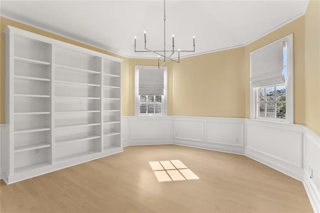 unfurnished dining area with built in shelves, ornamental molding, a chandelier, and light hardwood / wood-style flooring