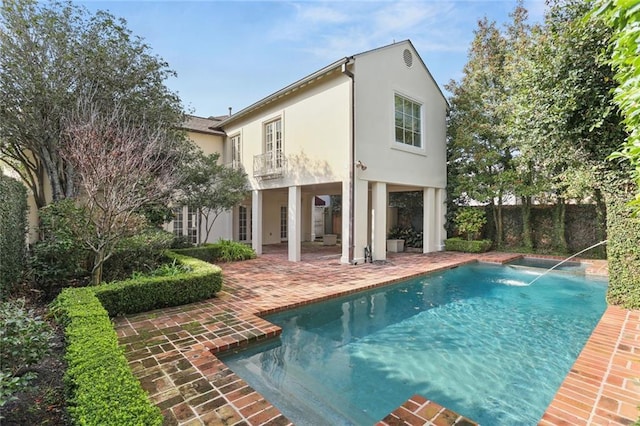 rear view of property with pool water feature, a balcony, and a patio area