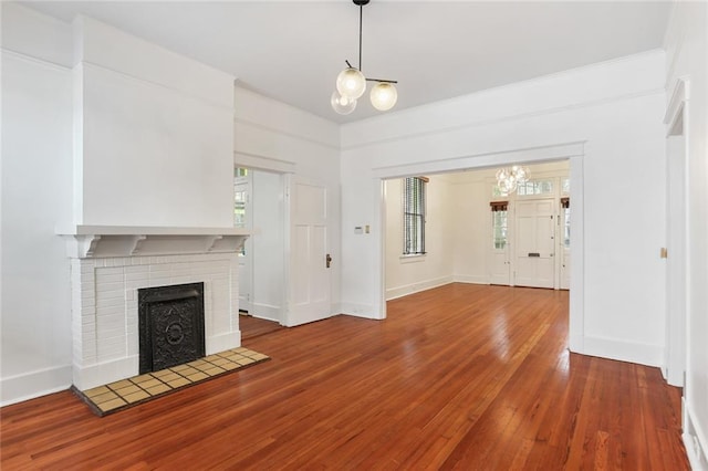 unfurnished living room with wood-type flooring, a brick fireplace, a healthy amount of sunlight, and a chandelier