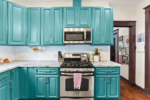 kitchen with blue cabinets, light stone counters, dark hardwood / wood-style floors, and appliances with stainless steel finishes