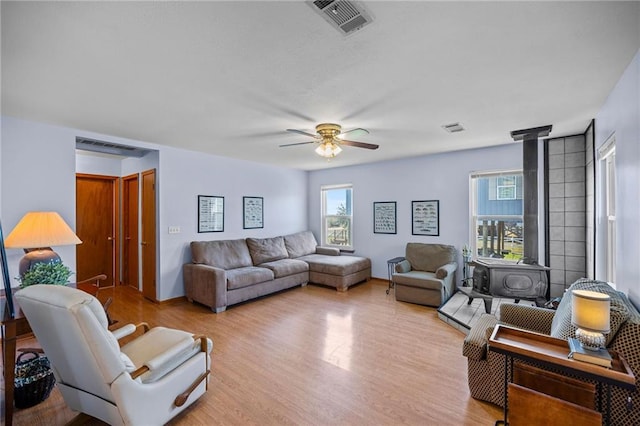 living room featuring ceiling fan, light wood-type flooring, and a wood stove