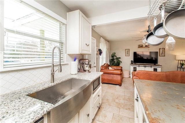 kitchen with sink, ceiling fan, light stone countertops, white cabinets, and decorative backsplash