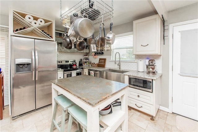 kitchen with sink, stainless steel appliances, light stone countertops, a kitchen island, and decorative backsplash